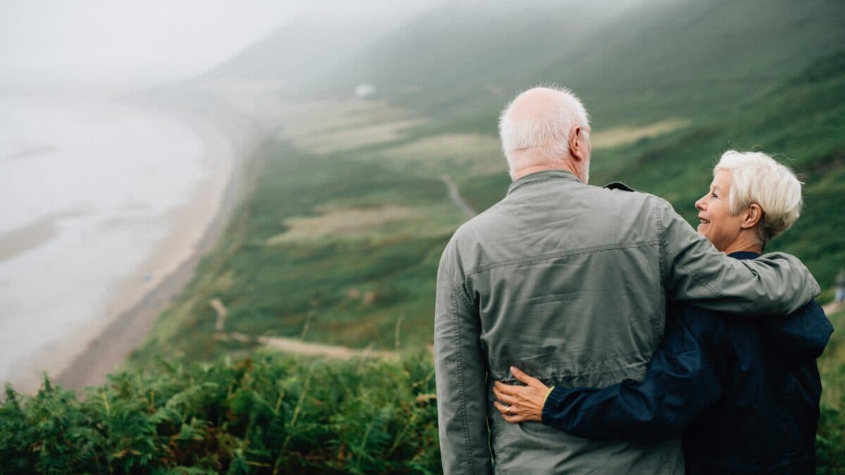 an elderly couple standing together on a hilltop, holding each other