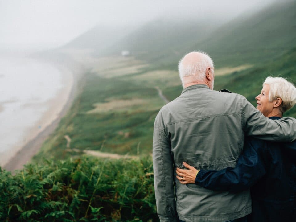 an elderly couple standing together on a hilltop, holding each other