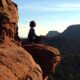 A woman meditating on the edge of a canyon, facing the sun.