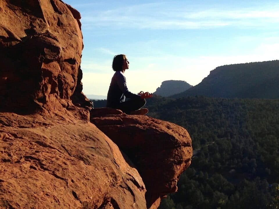 A woman meditating on the edge of a canyon, facing the sun.