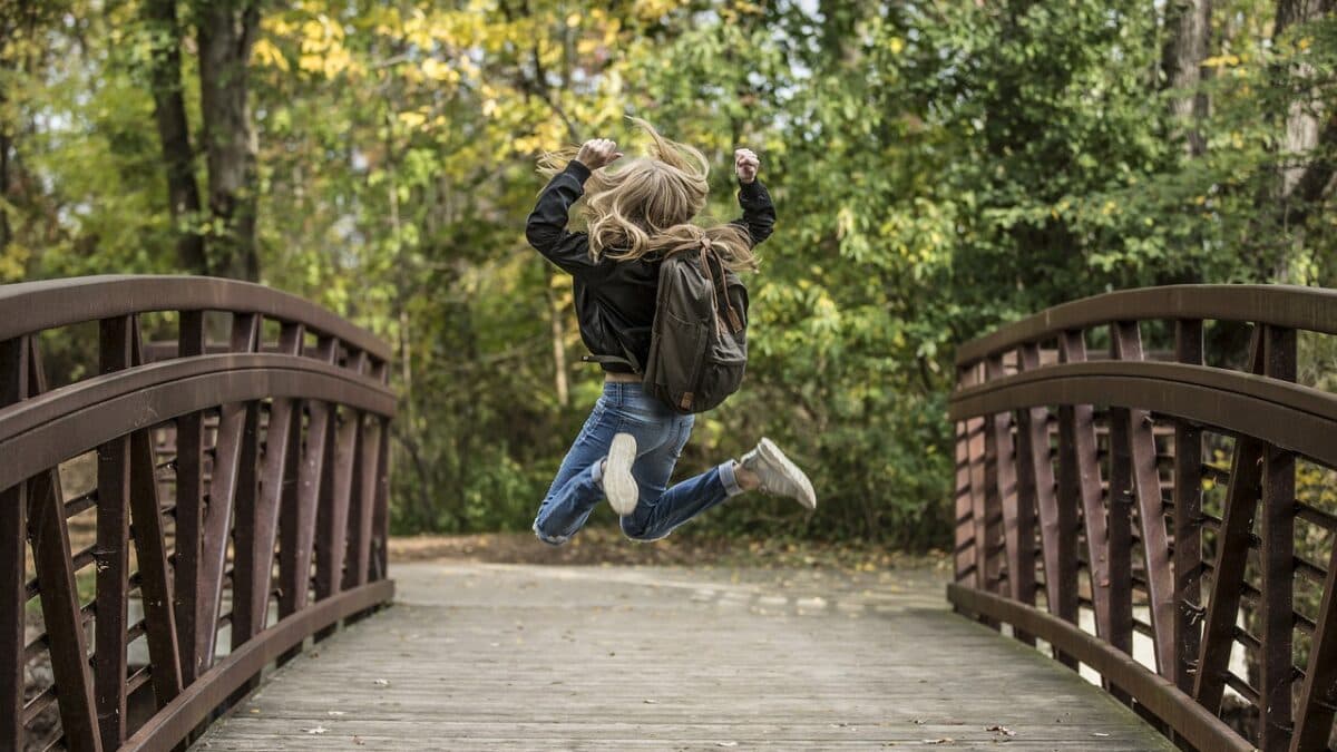 A woman joyfully jumping on a rustic wooden bridge in the middle of a lush forest