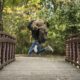 A woman joyfully jumping on a rustic wooden bridge in the middle of a lush forest