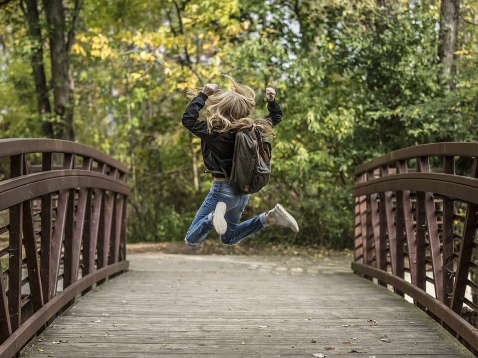 A woman joyfully jumping on a rustic wooden bridge in the middle of a lush forest