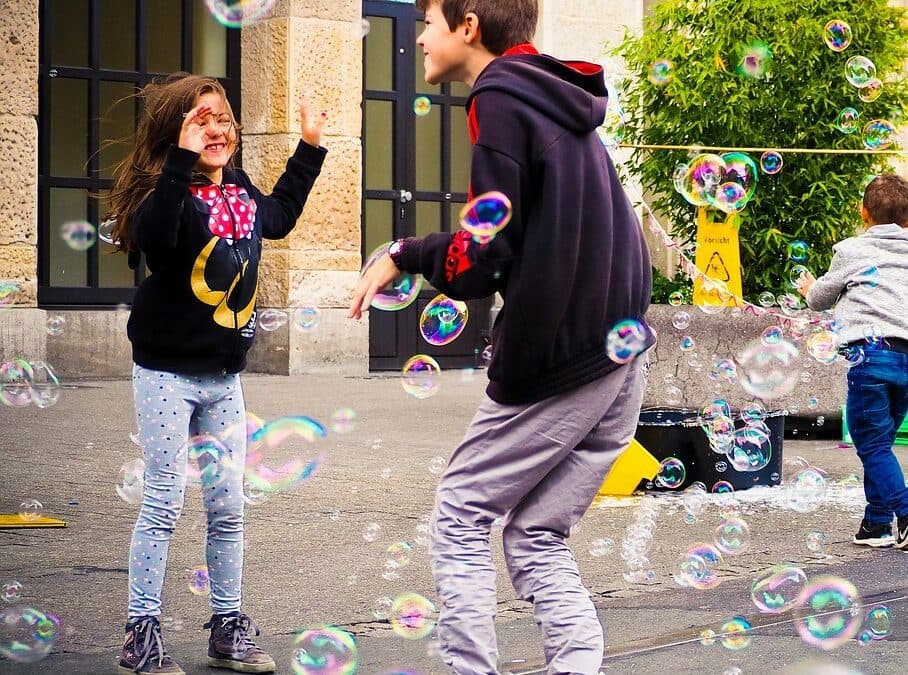 girl and boy kids playing together with bubbles in the street