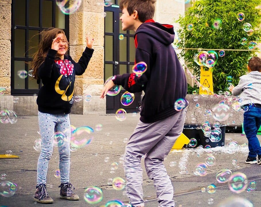 girl and boy kids playing together with bubbles in the street
