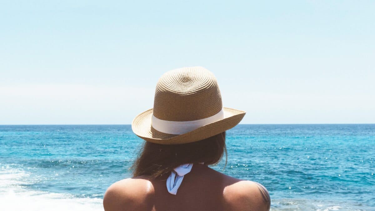 a woman with a hat facing the sea under the sun