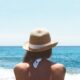 a woman with a hat facing the sea under the sun