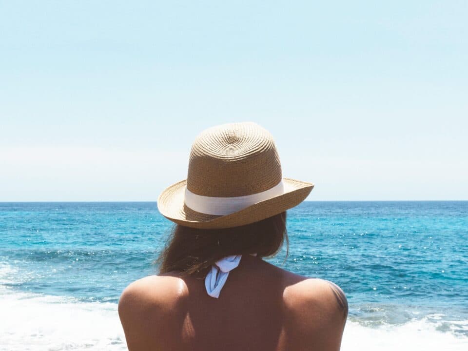 a woman with a hat facing the sea under the sun