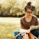 a woman sitting outside in the grass writing in a notebook