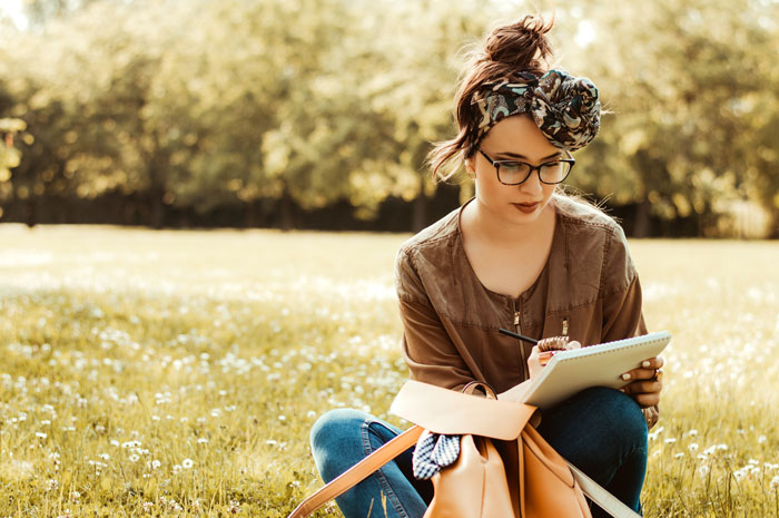 a woman sitting outside in the grass writing in a notebook