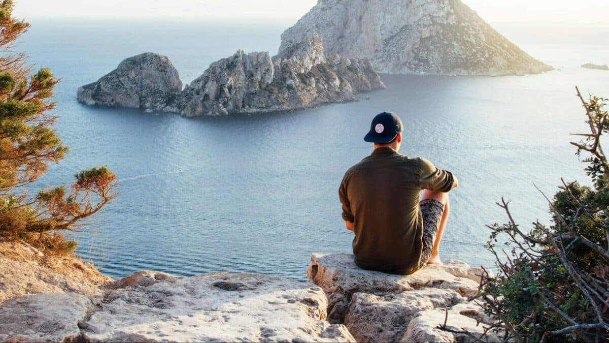 person sitting on edge of rocky plateau facing a body of water
