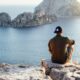 person sitting on edge of rocky plateau facing a body of water