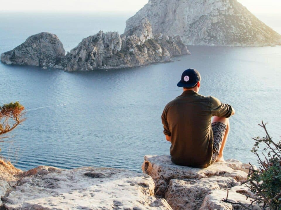 person sitting on edge of rocky plateau facing a body of water